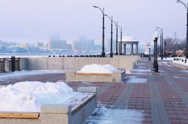 Kışın çiçek tarhlı bir bank, kar yığınıyla dolu. Rıhtımda Rotunda ve deniz feneri. Arka planda Çin 'in Heihe kenti bulanık. Blagoveshchensk, Rusya.