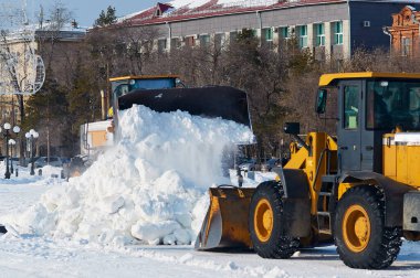 Yoldan kar kaldırma. Blagoveshchensk, Rusya 'daki bir sokaktan iki traktör grevcisi kar temizliyor. Kamu hizmetleri. Şiddetli kar yağışı sonucu. Kış güneşli gün.