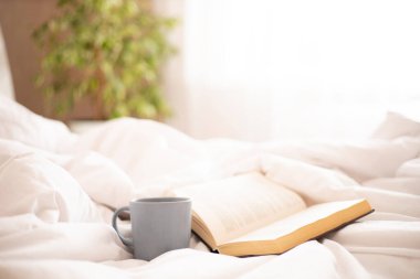 - Günaydın. Yatağın üzerinde bir kitap, bir kupa kahve ve çay. Pencerede güneş ışığı var. Rahatlatıcı. Atmosfer. Yaşam tarzı. Yüksek kalite fotoğraf