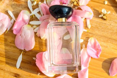 Yumuşak güneş ışığında, taze gül yapraklarının üzerinde duran berrak bir parfüm şişesi.