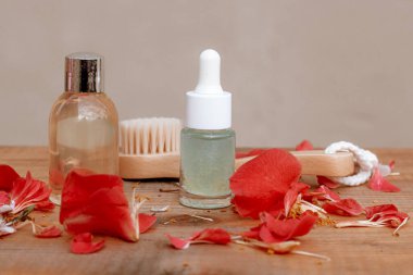 Esans yağı, vücut losyonu ve ahşap fırça taze gül yapraklarıyla masada duruyor.
