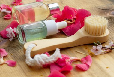  Tahta fırça ve doğal ahşap arka planda gül yapraklarıyla çevrili iki güzellik ürünü şişesi. Doğal kozmetik için fikir. Açı görünümü