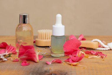 Düşürücü, ahşap kozmetik fırçası ve çiçek yapraklarıyla çevrili gerekli yağ şişesi.