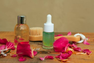 İki güzel ürün şişesi ve ahşap yüz fırçası taze gül yapraklarıyla masada duruyor.