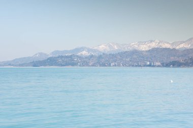 Uzakta karlı dağ zirveleri olan sakin mavi deniz. Deniz mavisi arka plan 