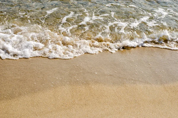 Deniz dalgalarının dokusu ve kumlu sahile yakın çekim.