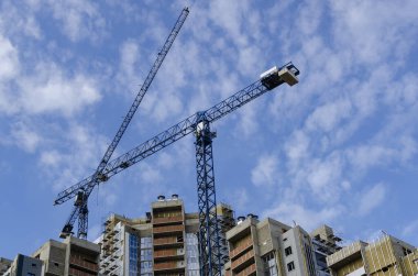 Çok katlı vinçlerin arasından yüksek bir binanın arka planına ve bulutlu bir gökyüzüne geçti..