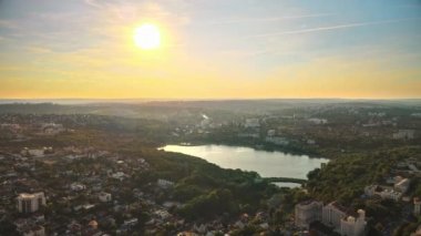 Chisinau 'nun günbatımında hava aracı görüntüsü. Yeşillik ve gölle dolu bir park. Birden fazla binanın panorama manzarası. Moldova
