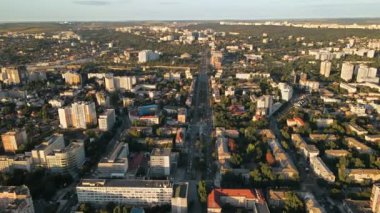 Chisinau 'nun gün batımında hava aracı görüntüsü. Birden fazla binanın manzarası, trafik ve yemyeşil ağaçlarla dolu bir yol. Moldova