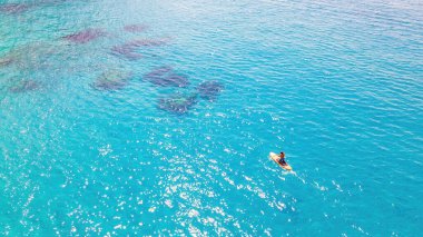 Yunanistan 'ın Zakynthos kıyısındaki bir teknede yüzen bir adamın insansız hava aracı görüntüsü. İyon denizinin mavi ve şeffaf suları