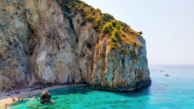 Yunanistan 'ın Zakynthos kentindeki İyon Denizi kıyılarının insansız hava aracı görüntüsü. Kayalık uçurum, bitki örtüsü, dinlenen insanlarla dolu plaj, mavi su.