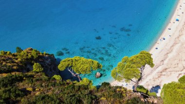 Yunanistan 'ın Zakynthos kentindeki İyon Denizi kıyılarının insansız hava aracı görüntüsü. Kayalık uçurum, bitki örtüsü, dinlenen insanlarla dolu plaj, mavi su. Dikey görünüm