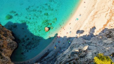 Yunanistan 'ın Zakynthos kentindeki İyon Denizi kıyılarının insansız hava aracı görüntüsü. Kayalık uçurum, bitki örtüsü, dinlenen insanlarla dolu plaj, mavi su. Dikey görünüm