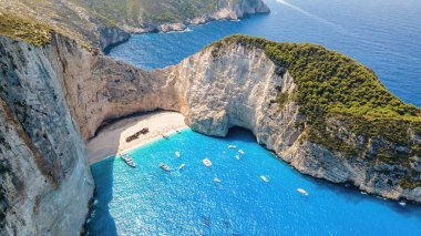 Yunanistan 'ın Zakynthos kentindeki İyon Denizi kıyısındaki Navagio plajının insansız hava aracı görüntüsü. Kayalık kayalıklar, demirli kayıklar ve dinlenen insanlar, mavi su