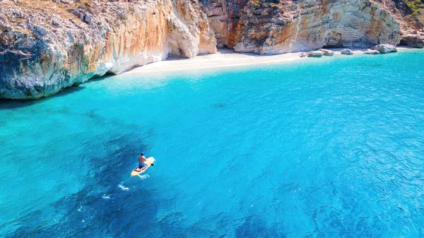 Yunanistan 'ın Zakynthos kıyısındaki bir teknede yüzen bir adamın insansız hava aracı görüntüsü. İyon denizinin mavi ve şeffaf suları