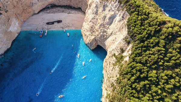 Yunanistan 'ın Zakynthos kentindeki İyon Denizi kıyısındaki Navagio plajının insansız hava aracı görüntüsü. Kayalık kayalıklar, demirli kayıklar ve dinlenen insanlar, mavi su