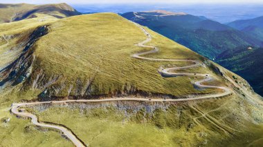 Romanya 'da doğanın insansız hava aracı görüntüsü. Karpat Dağları, seyrek bitki örtüsü, arabalı yol