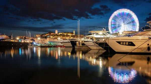 CANNES, FRANCE - 24 AĞUSTOS 2021: Demirlemiş yatlar, toprak döşeme sokağı, dönme dolap, gece lambaları.