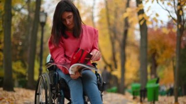 CHISINAU, MOLDOVA - 20 EKİM, 2021: Parktaki engelli sandalyesinde oturan kadın dergi okuyor