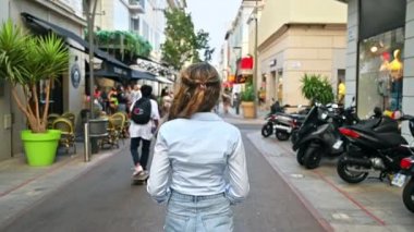 CANNES, FRANCE - 28 AĞUSTOS 2021: Yürüyen bir kadının arka görüntüsü, yürüyen insanlar, park etmiş scooterlar, kafeler