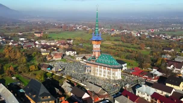 Aerial drone view of The Merry Cemetery in Sapanta, Romania. Church and multiple tombstones, visitors, residential buildings, yellowing trees