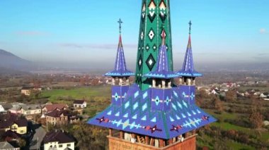 Romanya 'nın Sapanta kentindeki Merry Mezarlığı' nın insansız hava aracı görüntüsü. Kilise kulesi, konut binaları ve arka planda sarı ağaçlar.