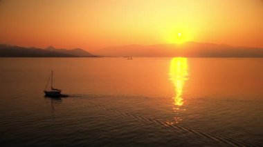 Yunanistan 'ın İyon Denizi kıyısında gün batımı. Parlak güneş, uzak bir yere iniş, yüzen tekneler, suda yansımalar.