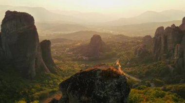 Meteora 'nın günbatımında Yunanistan' daki hava aracı görüntüsü. Ortodoks manastırlı kaya oluşumları. Bir sürü yeşillik, kutsal bir yer, arabalı yollar.