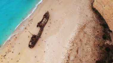 Yunanistan 'ın Zakynthos kentindeki İyon Denizi kıyısındaki Navagio plajının insansız hava aracı görüntüsü. Demir atmış gemi, dinlenen insanlar, paslı gemi, mavi su. Yavaş çekim