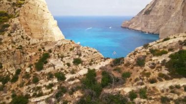Yunanistan 'ın Zakynthos kentindeki İyon Denizi kıyısındaki Navagio plajının insansız hava aracı görüntüsü. Demir atmış tekneler, dinlenen insanlar, paslı gemi, mavi su. Yavaş çekim