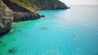 Yunanistan 'ın Zakynthos kıyısındaki bir teknede yüzen bir adamın insansız hava aracı görüntüsü. İyon denizinin mavi ve şeffaf suları