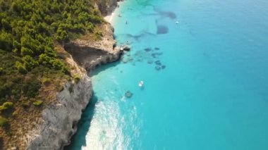 Yunanistan 'ın Zakynthos kentindeki İyon Denizi kıyılarının insansız hava aracı görüntüsü. Kayalık uçurum, bitki örtüsü, birkaç dinlenen insan, demirlemiş tekneler, mavi su