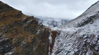 Romanya 'da doğanın insansız hava aracı görüntüsü. Karpat dağlarında transfagarasan rotası, dağlarda kar kayalık yamaçlar, bulutlar