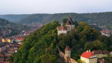 Romanya 'nın Sighisoara Tarih Merkezi' nin insansız hava aracı görüntüsü. Eski binalar, tepedeki kilise, yeşilliklerle çevrili.