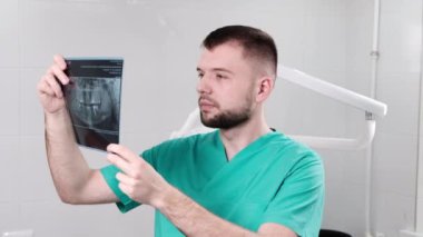 Diş muayenehanesindeki doktor röntgen testini kontrol edip açıklıyor.