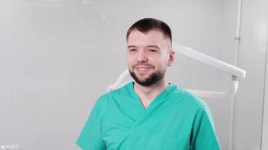 Doktor diş muayenehanesinde kameraya bakıyor ve gülümsüyor.