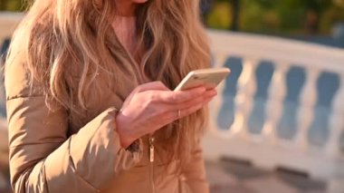 CHISINAU, MOLDOVA - Kasım 03, 2021: Gün batımında bir parkta beyaz bir iPhone üzerinde çalışan kadın