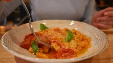 Restoranda domatesli İtalyan gnocchi yiyen bir kadın.