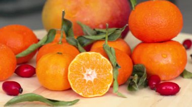 Dilimlenmiş portakal, mango, gül ağacı ve yeşil yapraklı kompozisyon, su damlacıklarıyla yakın plan.