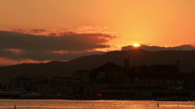 Günbatımında Fransa 'nın Cannes kentinde Akdeniz sahili manzarası. Güneş ufukta beliriyor, kumsal, binalar
