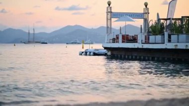 CANNES, FRANCE - 31 Ağustos 2021: İskeleli Akdeniz kıyıları, arka planda yatlar, günbatımı