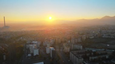 Romanya 'nın güneş doğarken Brasov' un insansız hava aracı görüntüsü. Arabalı yollar, konut binaları, sarı ağaçlar, arka planda Karpatlar..