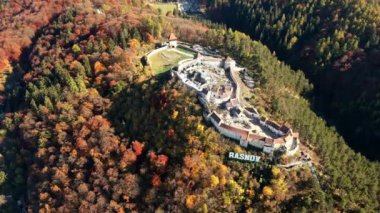 Romanya 'daki Rasnov Kalesi' nin insansız hava aracı görüntüsü. Tepenin tepesinde Rasnov yazıları olan ortaçağ kalesi, turistler. Yavaş çekim