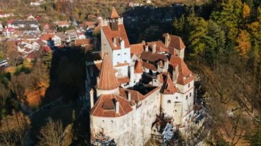 Romanya 'daki Bran Kalesi' nin insansız hava aracı görüntüsü. Karpatlar 'daki ortaçağ şatosu, sararmış ağaçlar, turistler, köy. Yavaş çekim