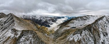 Romanya 'daki hava aracı doğaya panoramik açıdan bakıyor. Karpat dağlarındaki transfagarasan rotası, karla kaplı kayalık yamaçlar, vadi, bulut