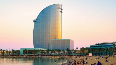 BARCELONA, İSPAN - 9 Haziran 2021 Akdeniz kıyısında gün batımında plaj. Birçok insan, otel ve avuç içi.