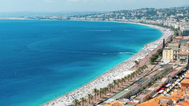 Nice, Fransa 'daki Cote d' Azur manzarası. Sahilde dinlenen insanlar, binalar, denizin mavi suyu, arka planda tepeler.