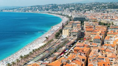 Nice, Fransa 'daki Cote d' Azur manzarası. Sahilde dinlenen insanlar, binalar, denizin mavi suyu, arka planda tepeler.