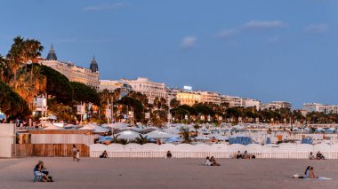 CANNES, FRANCE - 31 AĞUSTOS 2021: Günbatımında, sahil şeridinde, gece lambalarında, sıra sıra binalarda insanlarla dolu plaj