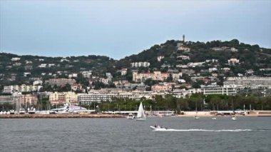 Fransa 'da yüzen bir tekneden Cannes manzarası. Geleneksel tarzda yapılmış binalar, yeşillik, tekneler. Yavaş çekim